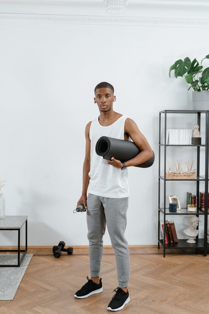 Young man holding yoga mat in a modern home gym setting, ready for workout.